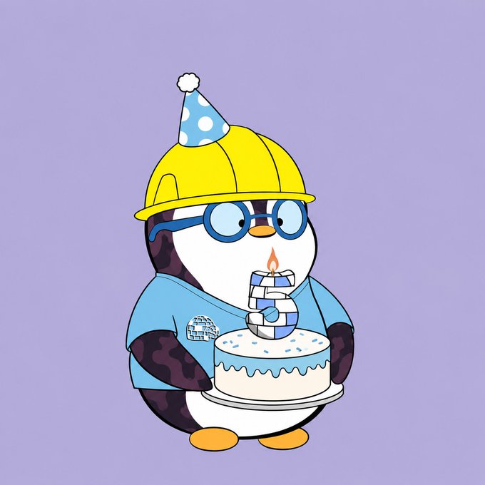 A cartoon penguin mascot wearing a yellow hard hat, party hat, and glasses holds a birthday cake with a candle shaped like the Pudgy Penguins logo, set against a purple background. The image illustrates the post's celebration of a Pudgy Penguins IRL milestone, with the cake and festive hat commemorating the "first ever Pudgy IRL" anniversary.