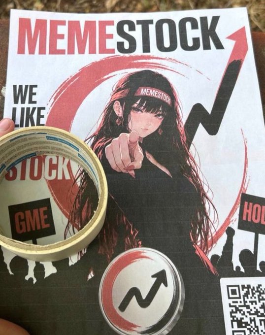 A 'MEMESTOCK' poster featuring an anime-style girl pointing at the viewer, accompanied by a roll of tape and a pin or coin bearing a rising arrow stock chart logo.