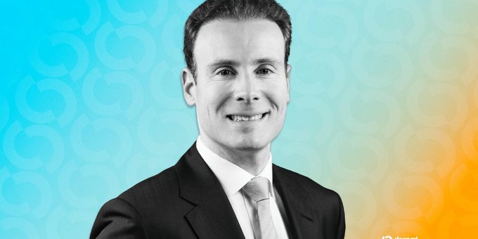 A black-and-white portrait of a smiling man in a suit and tie against a teal and orange gradient background with subtle circular patterns.