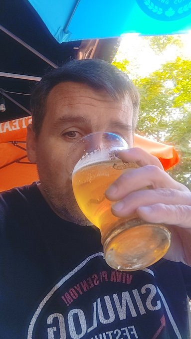iced tea with a frothy white head, held by a man wearing a black t-shirt and an "S" on his shirt.