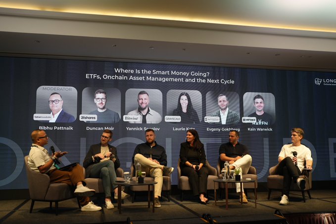 A panel discussion at what appears to be a crypto/blockchain conference titled 'Where Is the Smart Money Going? ETFs, Onchain Asset Management and the Next Cycle,' featuring moderator Shibhu Pattnaik and panelists Duncan Moir, Yannick Smoov, Laurie Katz, Evgeny Gokhberg, and Kain Warwick, with sponsor logos for 21Shares, Binance, Mantra, Hyperliquid, and Kraken visible on the screen.