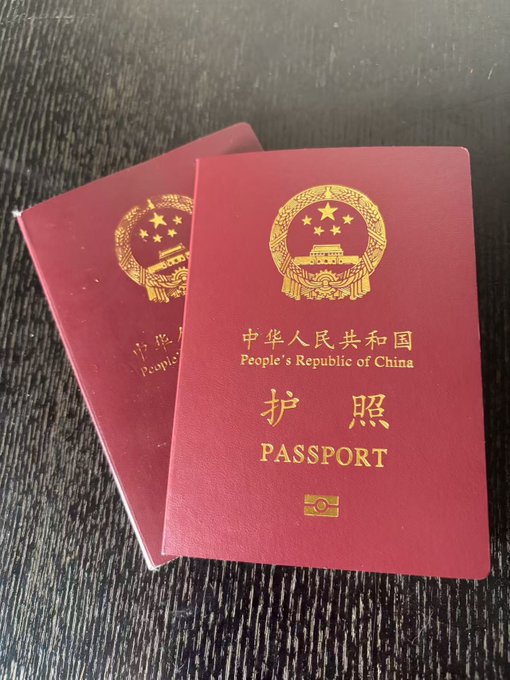 Two red passports for the 'People's Republic of China' with the Chinese characters '护照' (Passport) and the national emblem, resting on a dark wooden surface.
