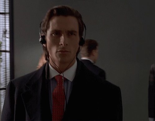 The image features a man wearing headphones, possibly listening to music or taking an important call while dressed in a suit. The background shows another person who appears to be a woman with a red tie. There are also two other people partially visible in the scene. The image is related to the post because it discusses the importance of verifying game ratings and reviews, which can be compared to verifying the authenticity or credibility of information presented in the image.
