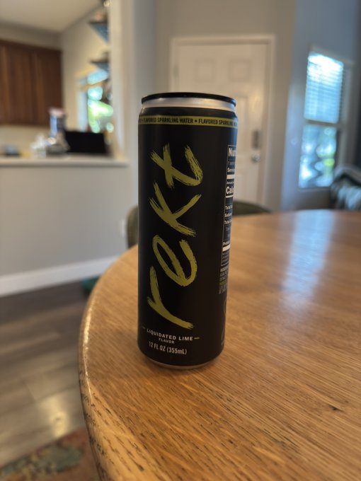 A black can of 'YOXK' liquidated lime flavored sparkling water sitting on a wooden table, with a kitchen visible in the background.