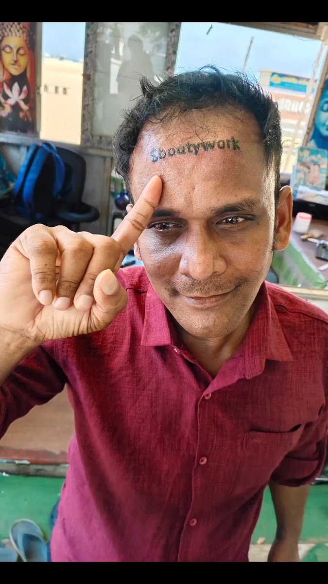A man wearing a red shirt is holding up his finger with a thumbs-up gesture, indicating that he supports or endorses the idea of getting a forehead tattoo for $32,500. The image appears to be taken at a store named "Forehead Crypto Tattoo", which focuses on offering wild challenges and tattoos.