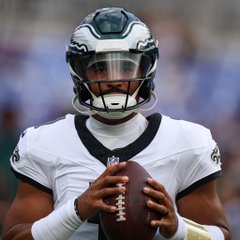 Philadelphia Eagles quarterback Jalen Hurts in a white jersey holds a football during an NFL game.