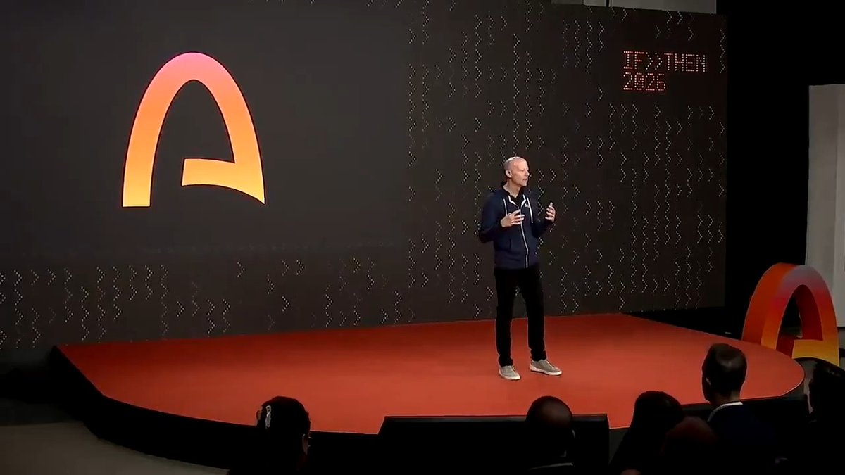 A speaker stands on a red stage in front of a large screen displaying the Arc logo and "IF/THEN 2025" during the Arc Mainnet launch event, announcing the network is now live.