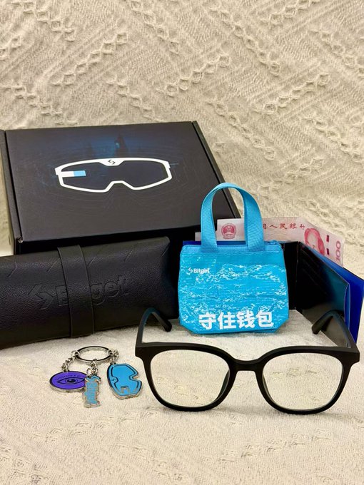 The image shows a pair of glasses resting on top of a black box with a blue label that says "Unboxing reveals a hundred-yuan bill." The glasses are placed next to a wallet and a keychain, which appear to be made out of paper. A small bag is also present in the scene. The post seems to be about an Unboxing experience or a recent delivery, possibly related to money or other valuable items.