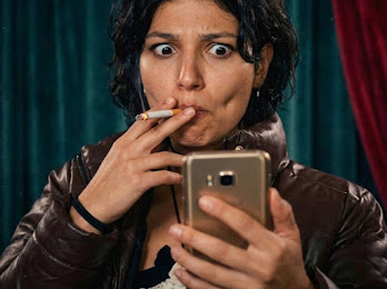 The image shows a woman holding a smartphone, with her mouth open as if she's about to make a funny face or give a speech. The background features a green curtain that matches the color of the eyeshadow worn by the woman. The caption "Someone just rub the algo g spot Now it's wet and coming" suggests that there might be an unexpected event happening, possibly related to the woman's phone usage.