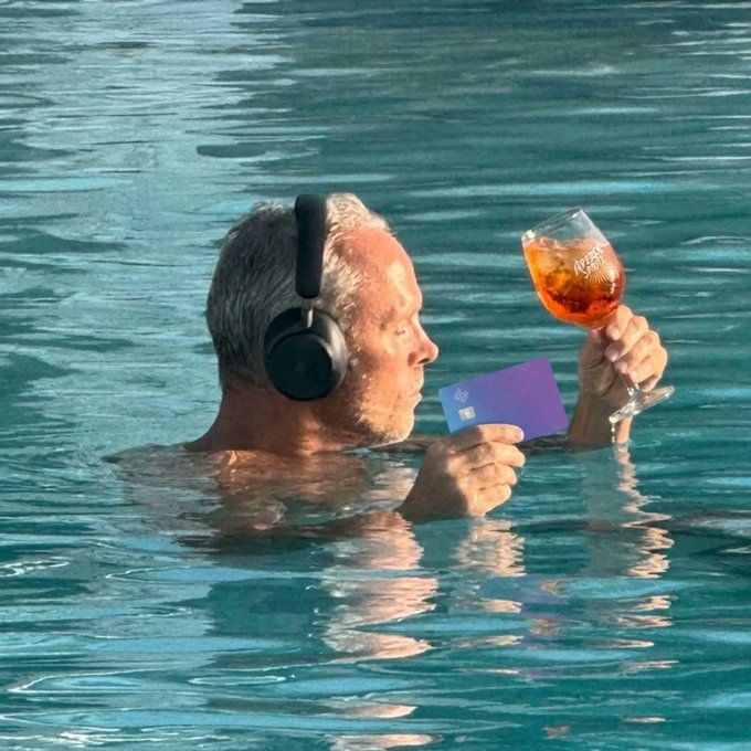 A man in headphones enjoys an Aperol Spritz and holds a purple EtherFi Cash card in a pool, embodying a worry-free "euro summer" experience. The image visually represents the advertised benefit of 0% FX fees for the EtherFi Cash card.