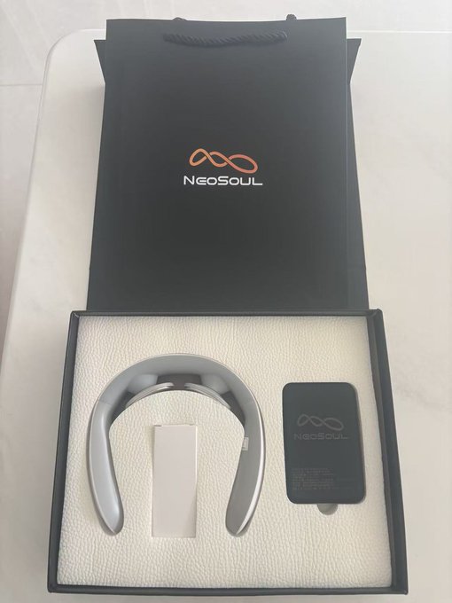 A NeoSoul branded box containing a silver neckband-style wearable device and a small black accessory, displayed on a white textured surface.
