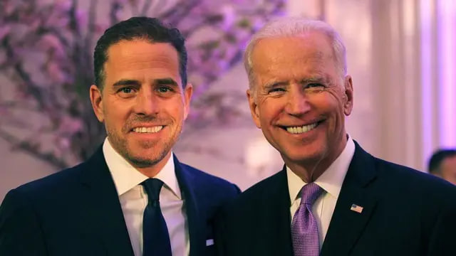 Two men in dark suits and ties smile for the camera at what appears to be a formal indoor event, with the older man wearing an American flag lapel pin, while the accompanying post mocks a $LAPTOP crypto token crash and taunts them about financial losses.