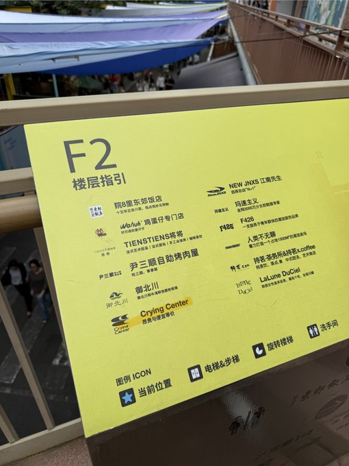 A yellow directional sign for 'F2' lists various shops and services, including 'TIENSTIENS 将将' and 'Crying Center', with Chinese characters indicating the floor guide.
