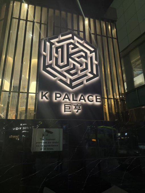 An illuminated sign for 'K PALACE 巨亨' features a geometric logo and indicates that the premises are under CCTV surveillance at all times.