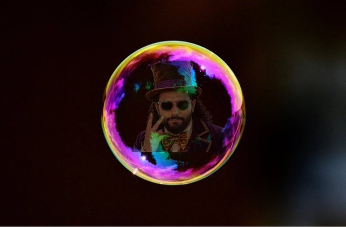 A vibrant, multicolored bubble floats in a dark space, containing an illustration of a bearded man in a top hat and sunglasses making a hand gesture.