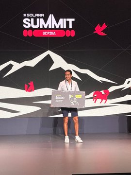 A man stands on stage holding a large novelty check for $5,000 at 'SOLANA SUMMIT SERBIA.'
