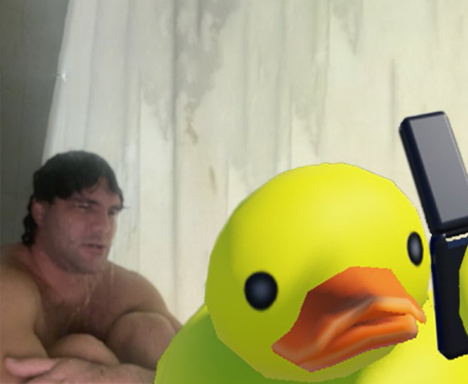 A 3D-rendered yellow duck with an orange beak appears superimposed in the foreground, with a man with dark hair sitting shirtless in the background behind a curtain.