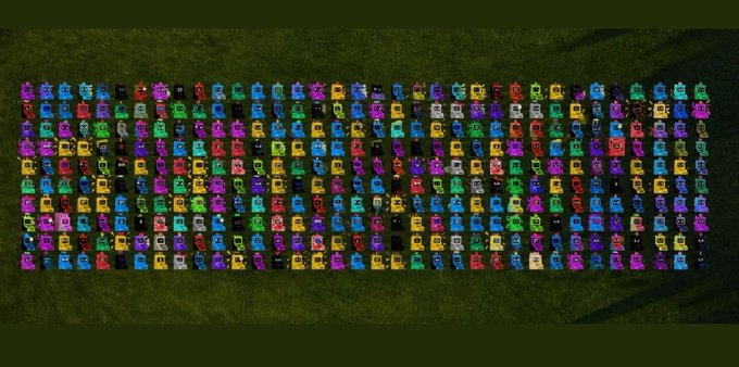 An aerial view of a large, organized grid of colorful (pink, blue, yellow, purple) plastic ride-on toys or playground equipment laid out on grass.