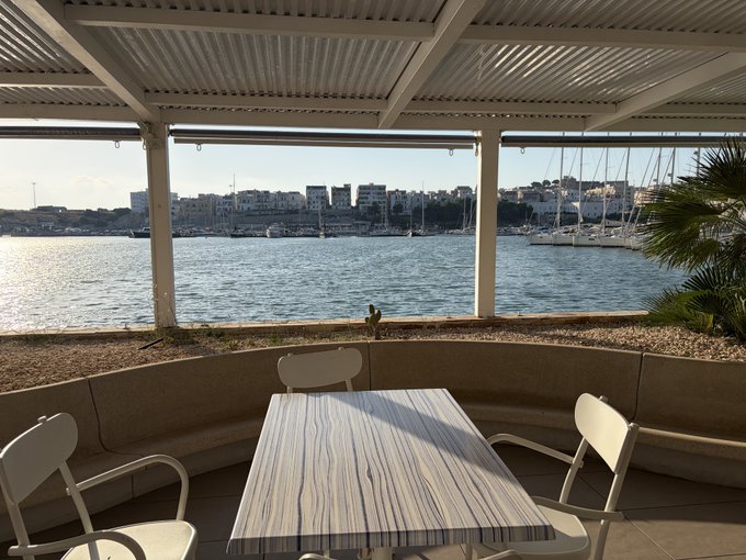 A view from a covered patio with a table and chairs overlooking a harbor filled with sailboats.