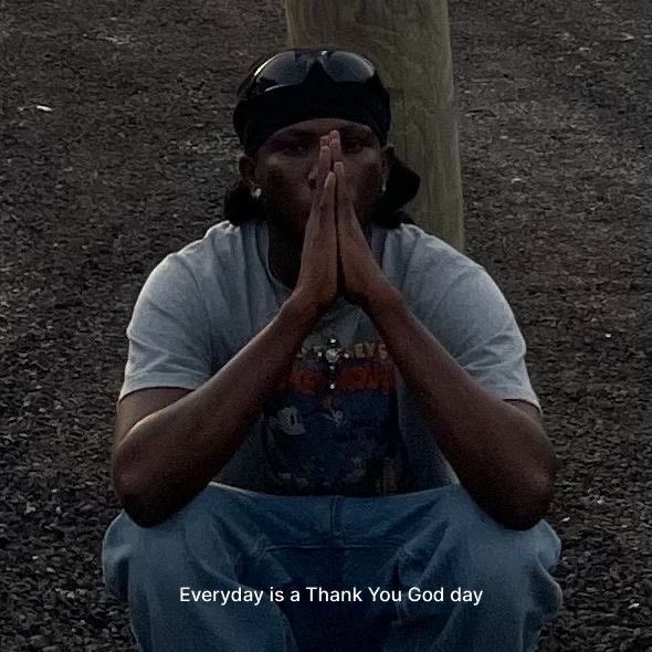 A person in a dark bandana and grey t-shirt sitting cross-legged with hands clasped in prayer, captioned 'Everyday is a Thank You God day.'