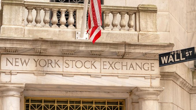 The facade of the New York Stock Exchange building is shown, with an American flag hanging above the engraved name and a Wall Street sign visible on the right.