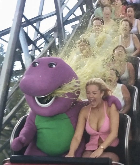 A photo from a roller coaster showing Barney the purple dinosaur mascot riding next to a screaming woman in a pink bikini top.