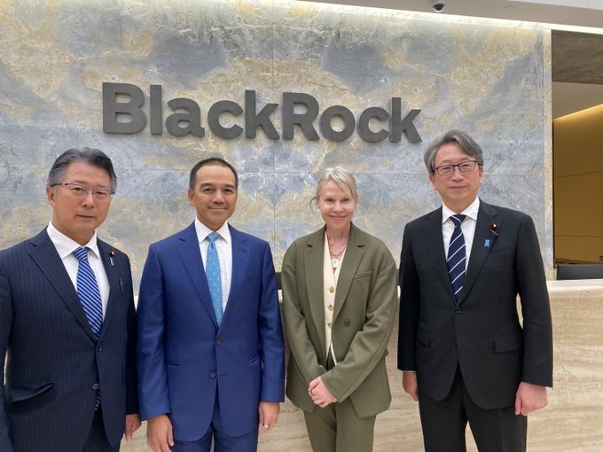 Four people in business attire pose for a photo in front of a marble wall with the 'BlackRock' logo.