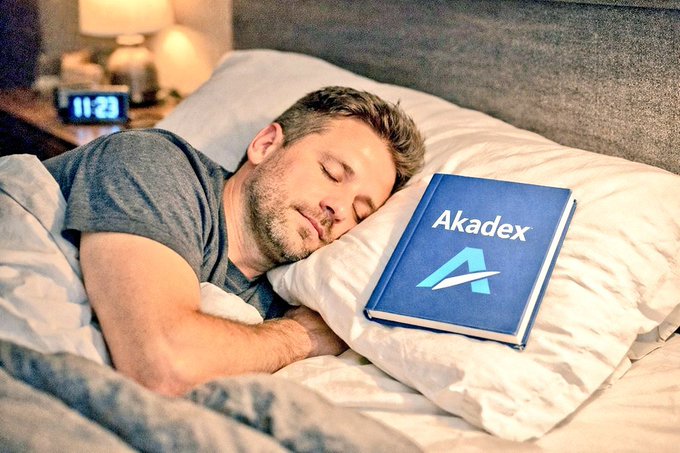 A man sleeping peacefully in bed next to a blue book titled 'Akadex' with an upward arrow logo, while a digital clock shows 11:27.
