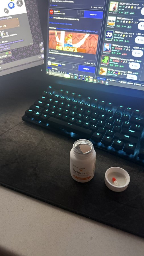 A casual desk setup photo shows a backlit mechanical keyboard in front of dual monitors displaying Discord chat and crypto listings, with an open white pill bottle of 'Cytotoc' and its cap resting on a black mousepad.