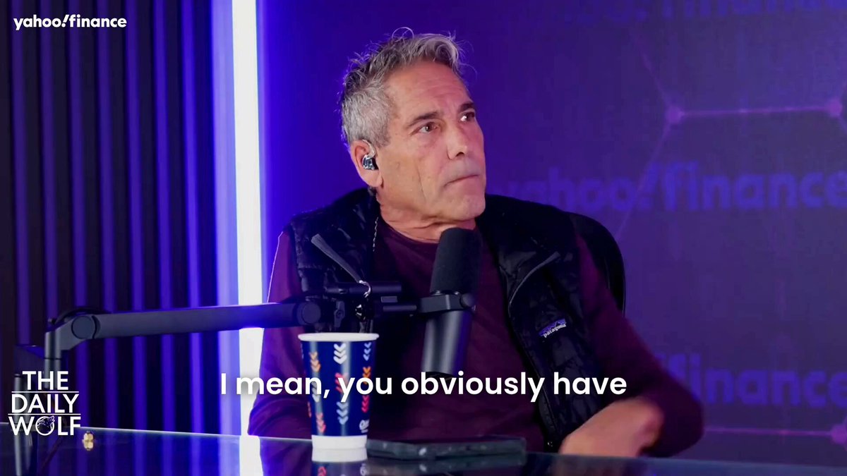 The image shows a man sitting at a desk with a microphone, wearing headphones, and holding a cup of coffee. The background features a purple wall with white text that reads "The Daily Wolf" and "Bitcoin's really taught me". The caption below the image states "I mean, you obviously have", suggesting an interesting conversation or idea related to Bitcoin.