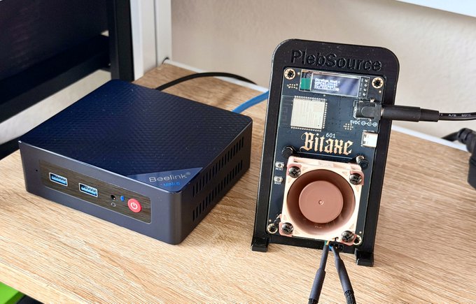 A Beelink mini PC sits next to a "Bitaxe 601" Bitaxe solo miner powered by "Plebsource," showcasing a compact home Bitcoin mining setup capable of running a node, mining pool, and miner.