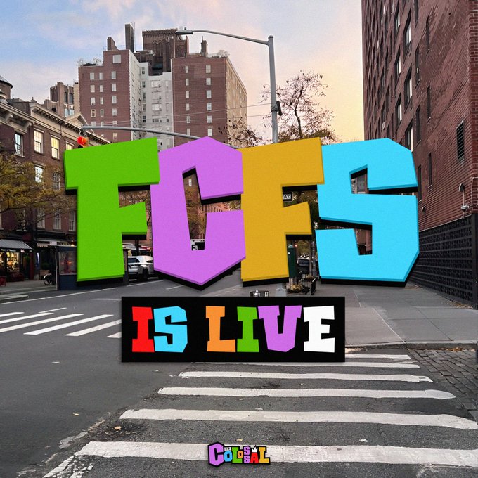 The image features a crosswalk with a colorful sign that reads "FCFS is now live". This suggests that the photo was taken during an event or gathering related to FCFS, possibly a protest or rally. The text "CATAL" can also be seen in the image, which might indicate the location of the event or the specific cause being addressed by the participants.

The background shows buildings and cars, indicating that this is likely taking place in an urban setting with traffic and infrastructure.