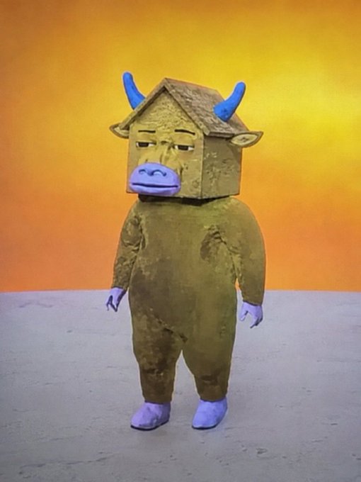 A surreal sculpture of a humanoid figure in an olive-green fleece bodysuit with a small house/shed for a head featuring blue horns, ears, and a horse-like snout, standing against an orange gradient background.