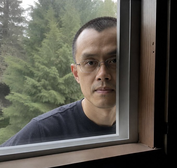 A self-portrait of an Asian man with glasses and short hair wearing a black shirt, photographed through a window frame with green trees visible in the background.