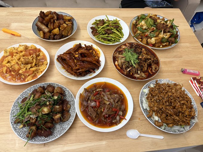 A spread of various Chinese dishes including braised pork, vegetables, seafood, and stir-fries arranged on a wooden dining table.