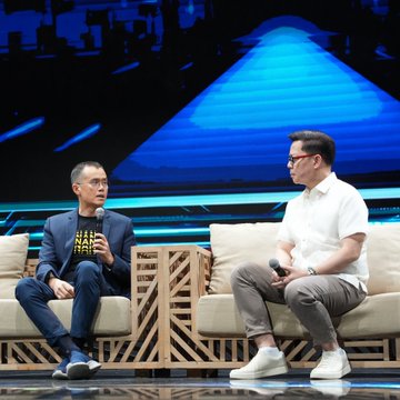 Two men sit on a stage in cushioned chairs during a panel discussion, with one wearing a black t-shirt displaying "HODL" and "HAPPI" while holding a microphone, and the other in a white polo shirt. The image illustrates the accompanying post about Binance founder Changpeng Zhao (CZ) speaking at the ASEAN Tech Summit Manila 2026 in the Philippines, advocating for crypto license passporting across ASEAN member states.