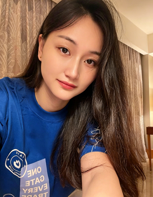 A selfie of a young woman with long dark hair wearing a blue t-shirt with a white smiley face logo and text reading 'ONE', 'GATE', 'EVERY', 'TASTE' (mirrored).