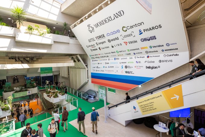 An indoor conference venue "WONDERLAND" features a large sponsor banner displaying numerous crypto/blockchain logos including Canton, Pharos, OneSiS, Ledger, and others above a green carpeted atrium.