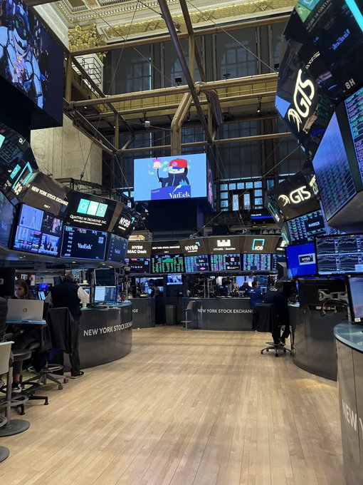The image shows the interior of the New York Stock Exchange trading floor, featuring numerous digital screens displaying financial data, with "Pudgy Penguins" prominently shown on a central screen alongside its "VanEck" ticker branding. The Pudgy Penguins logo is featured on one of the main display monitors, highlighting the brand's presence at this iconic financial venue.