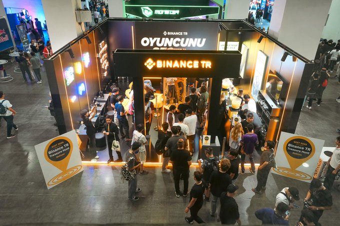 A bustling crowd gathers at the Binance TR "OYUNCUNU" booth at the Gaming Istanbul event, where attendees can be seen engaging with staff and exploring the promotional displays. The setup features prominent Binance TR branding and signage advertising ByNoGame digital code distribution for new users who complete registration and KYC procedures.