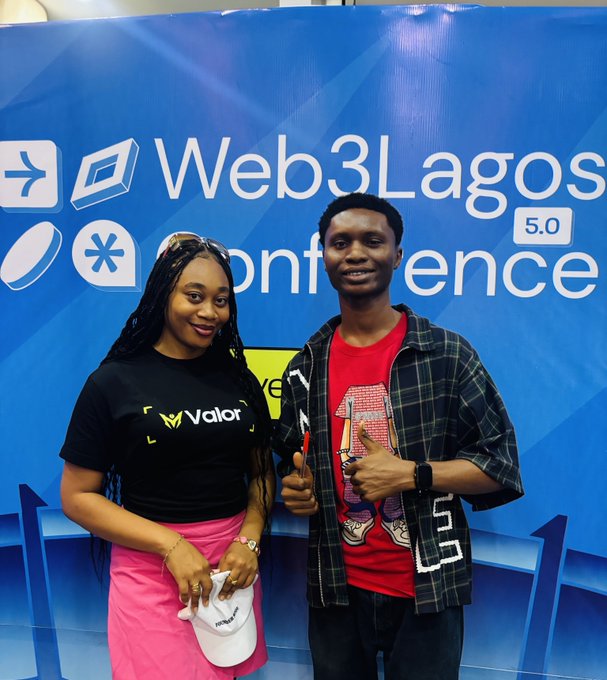 Two people posing and giving thumbs up in front of a blue Web3Lagos Conference 5.0 backdrop, with the woman wearing a Valor-branded shirt.
