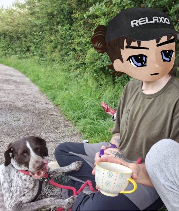 A person wearing a "RELAXIO" cap sits along an English countryside canal with their spotted dog, holding a colorful polka-dot cup of tea — capturing the essence of a peaceful, relaxed day on the towpath.