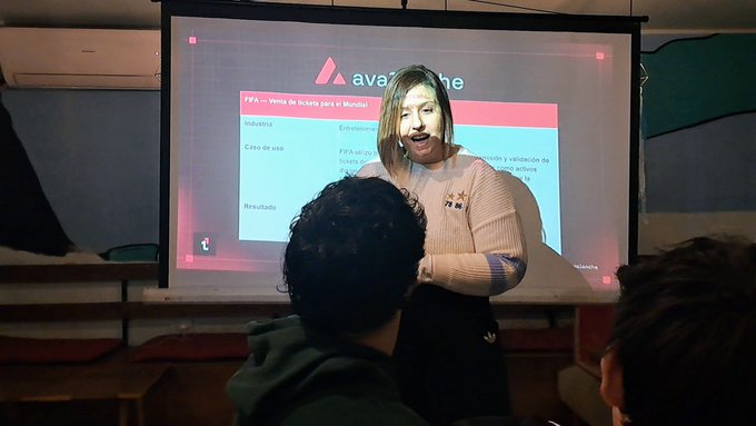 A young woman stands in front of a projector screen presenting on a topic, with the slide behind her titled 'PFA - Venta de tickets para el Mundial' (World Cup ticket sales).