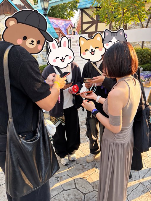 A group of people outdoors on a paved street holding phones and pins, with cartoon animal face stickers (bear, rabbit, dogs) covering their faces, and a partially visible 'DO NOT TRUST' sign.