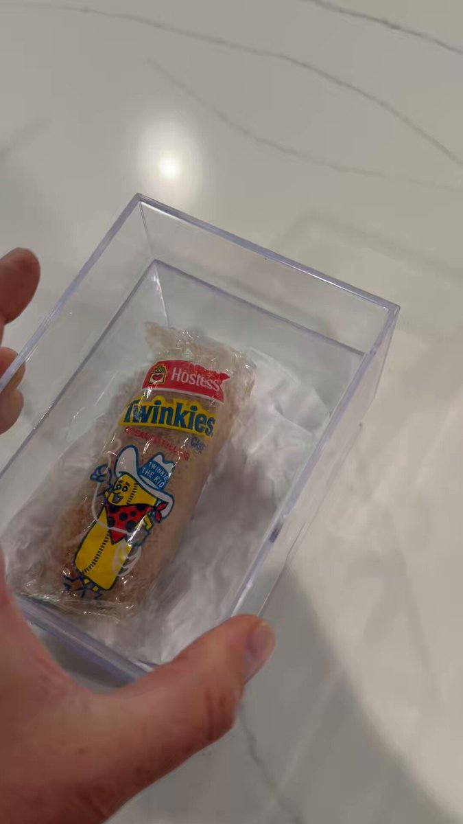 The image shows a person holding up a small package of Hush Kies candy, which has a cartoon character on it. The packaging appears to be made of clear plastic, making it easy to see the contents inside. In the background, there is a white countertop with a visible grain pattern. The post in the image seems to be about Bitcoin and cryptocurrency, suggesting that someone might have received this package as a gift or won it in an online contest related to Bitcoin.