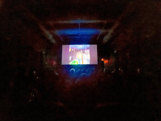 A dark, low-quality photo showing a projection screen in a dimly lit room displaying colorful, indistinct content.