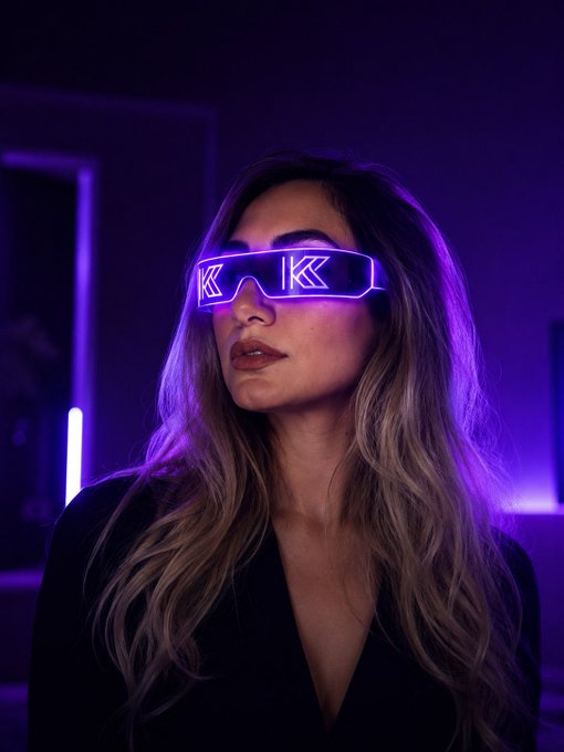 A stylized portrait of a woman wearing purple neon LED glasses with arrow designs, set against a dark purple-lit background.