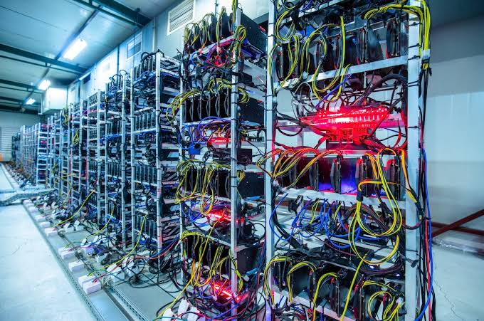 Rows of server racks filled with tangled yellow, blue, and black cables illuminate a data center with red and blue indicator lights.
