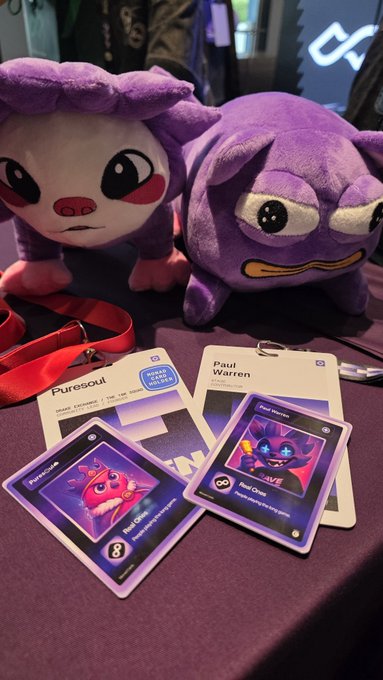 Two plush toys resembling apes/monkeys sit behind a lanyard with 'Puresoul' branding, displaying collectible cards featuring 'Puresoullite' and 'Red Onyx' characters.
