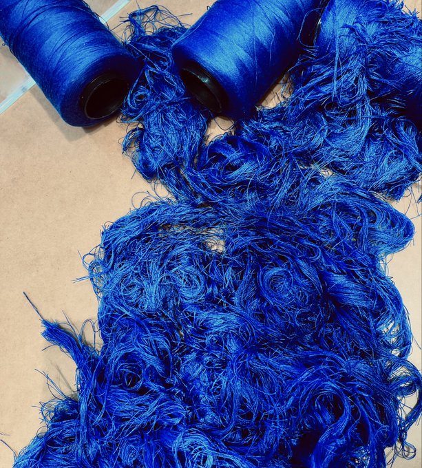 Spools of vibrant blue thread or yarn with loose strands spreading across a cardboard surface.